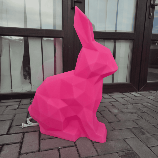 Pink geometric rabbit sculpture on a brick pavement