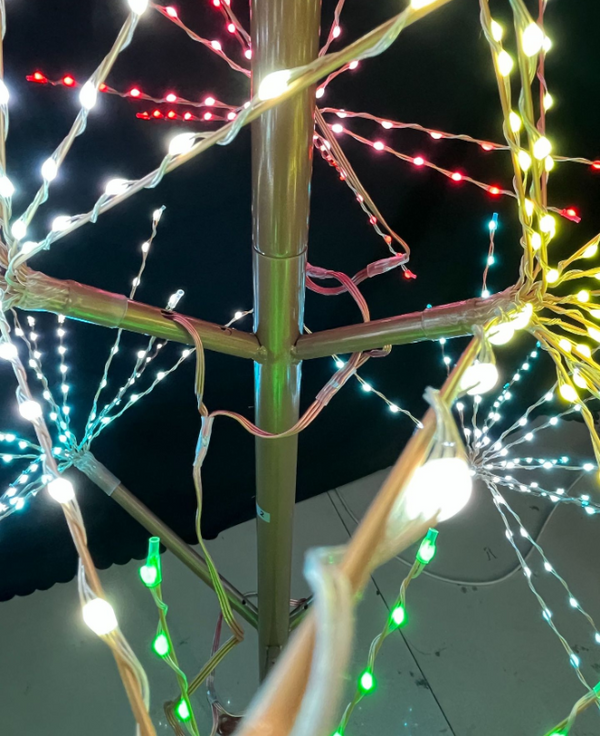 A LED Christmas light tree frame with multicolor starburst lights in red, green, blue, yellow, and white, photographed against a dark night sky.