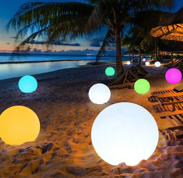 Colorful illuminated balls on a sandy beach with palm trees and a hut in the background.