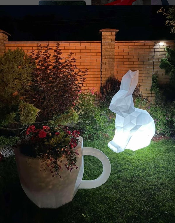 Glowing white rabbit-shaped light in a garden setting with a brick wall and plants.