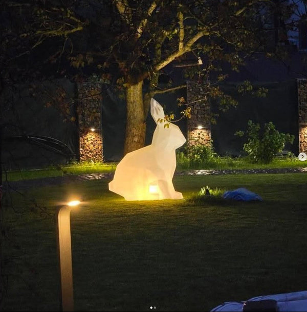 Glowing rabbit-shaped outdoor light in a garden setting at night.