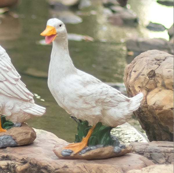 White duck statue on a rock with water and another duck in the background