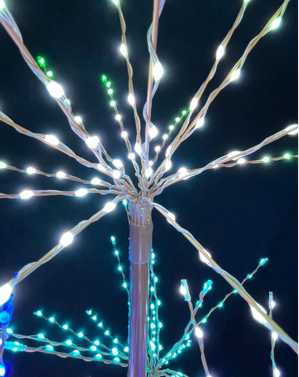 White and green LED branch-style string lights arranged on a central pole against a dark night sky.