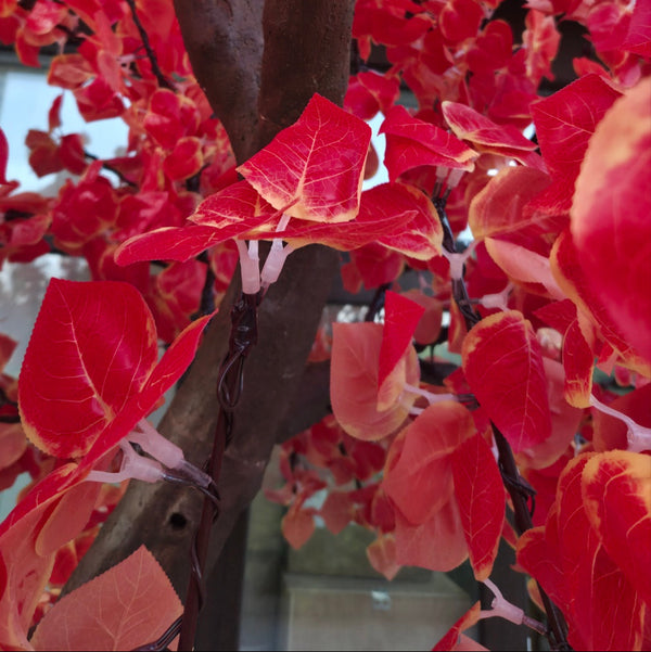 A close-up of a red artificial tree with bright red leaves and dark brown branches, photographed tightly with some leaves blurred in the foreground.