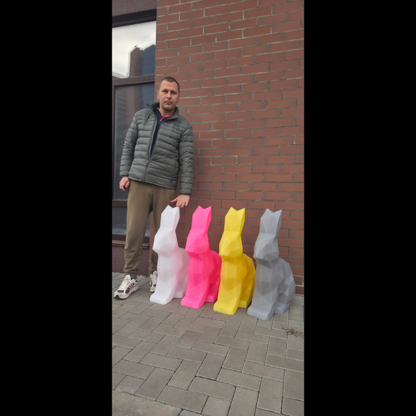 Man standing next to four colorful plastic bunny statues against a brick wall.