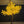 An artificial decorative tree with bright yellow glowing leaves and a brown trunk, mounted on a round black base in an indoor setting with a dark wall and metal ceiling.