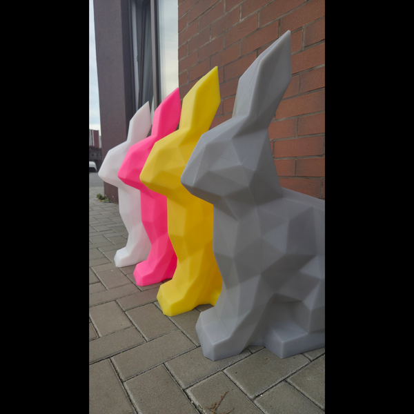 Colorful geometric rabbit sculptures on a pavement next to a brick wall.