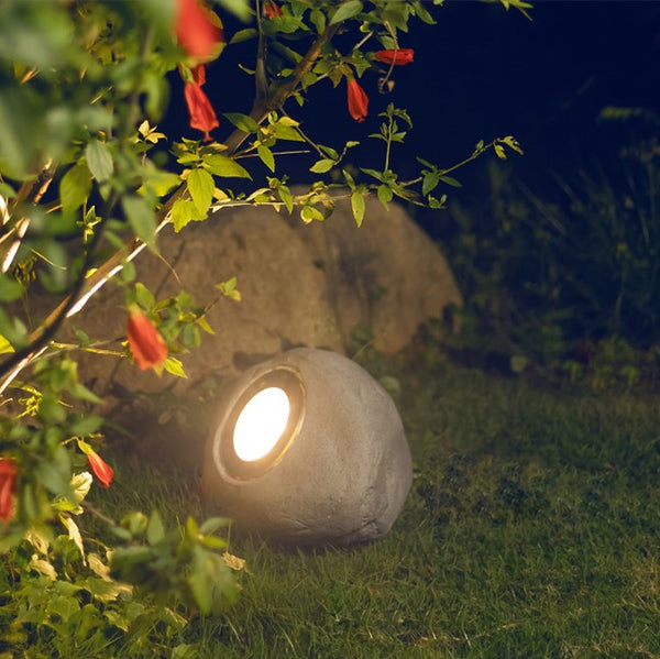 Cement garden light fixture on grass with red flowers and green leaves in the foreground