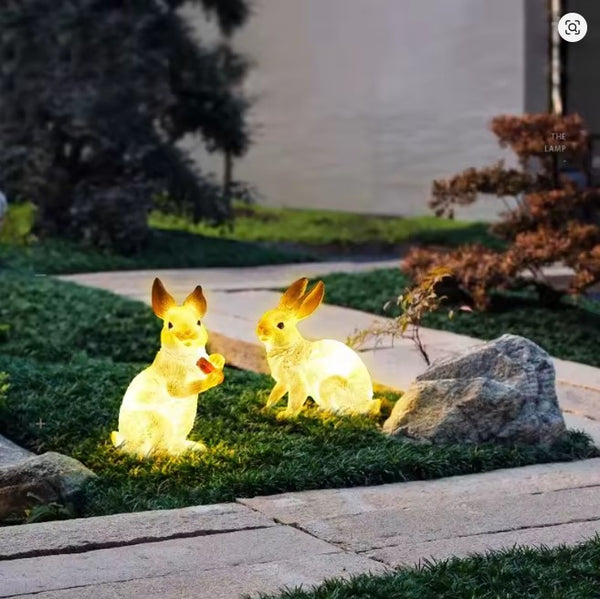 Two rabbit-shaped garden lights on grass with a building in the background