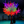 A large decorative tree with glowing multicolor LED lights in red, orange, yellow, green, blue, and purple, set in a dark indoor event space with other illuminated trees in the background.