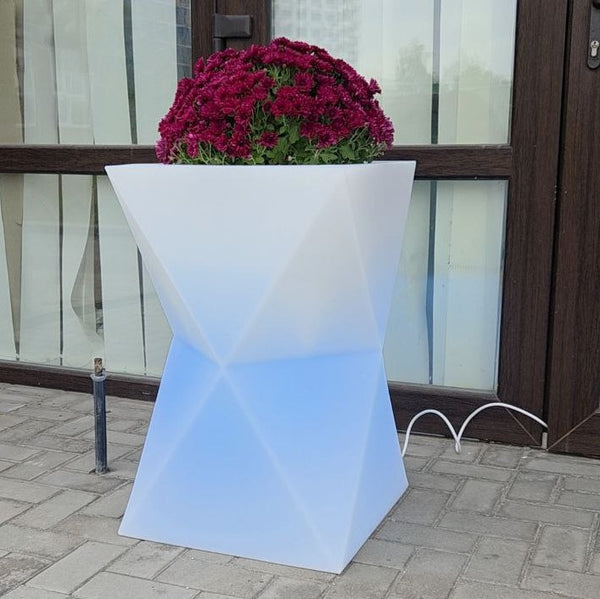 Vibrant RGB illumination of the Hourglass outdoor planter in a patio setting. Shows the 16-color LED lighting feature