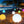 Colorful illuminated balls on a sandy beach with palm trees and a hut in the background.
