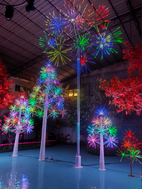 A set of illuminated LED decorative trees with colorful starburst branches, displayed in a large indoor event space with a reflective blue floor and high ceiling.