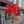 An artificial autumn tree with bright red and orange leaves on a brown trunk, staged on a sidewalk in front of a building with storefront windows.