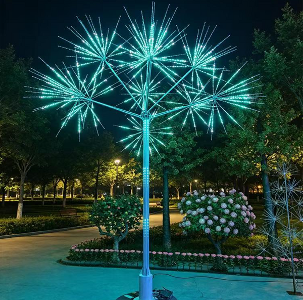 A large decorative LED tree light sculpture in a park at night, emitting bright turquoise-blue starburst branches from a central pole.
