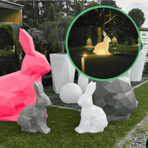 Geometric rabbit sculptures in various colors on a grassy area with a garden background.